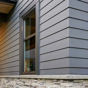 Todd Miller Roofing, Siding, and Seamless Gutters Sidng - click to view siding options and manufacturers; corner of house with grey blue siding and stone with one window